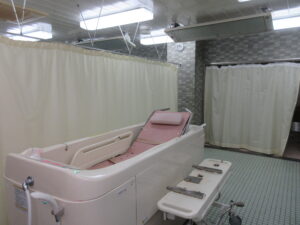 介護用の機械浴槽。ピンク色の浴槽と操作パネルが見える浴室。