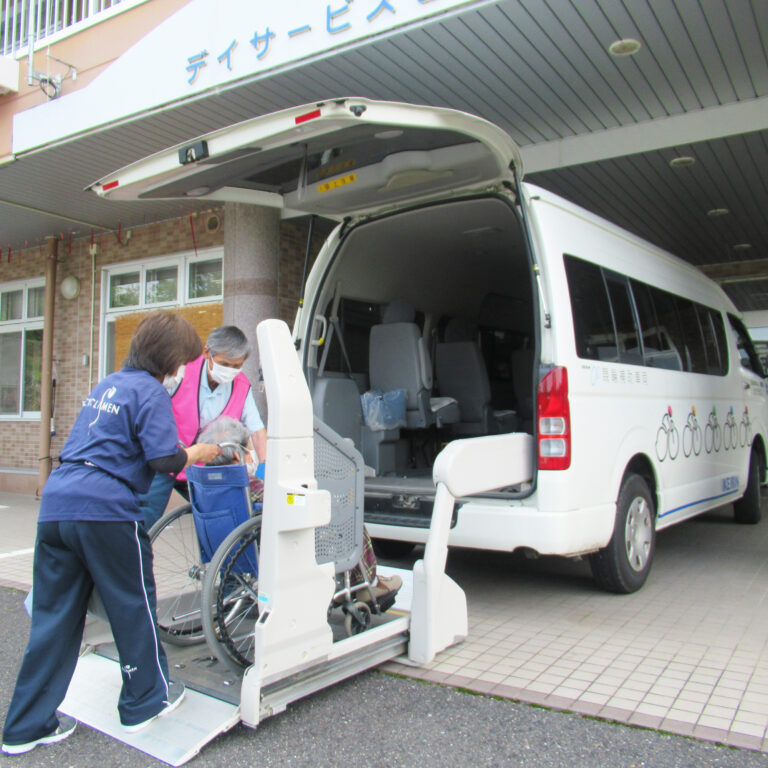 介護施設の送迎車へ車椅子利用者を乗せるスタッフの様子